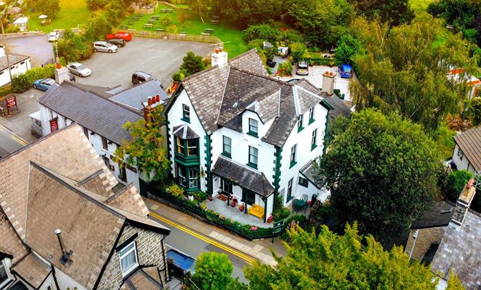 Large white and green house in Trefriw, North Wales seen from above surrounded by green trees and with green fields behind it